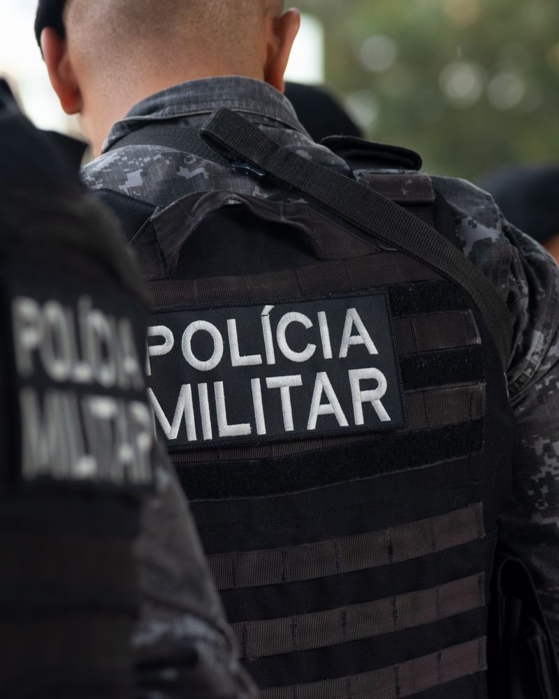 Policiais militares de costas, com a inscrição Polícia Militar no colete.