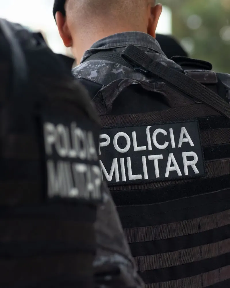 Policiais militares de costas, com a inscrição Polícia Militar no colete.