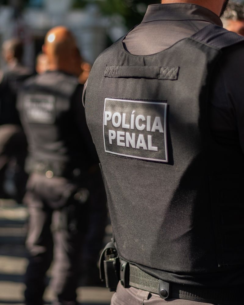 Policiais penais uniformizados em formação, com a inscrição Polícia Penal no colete.
